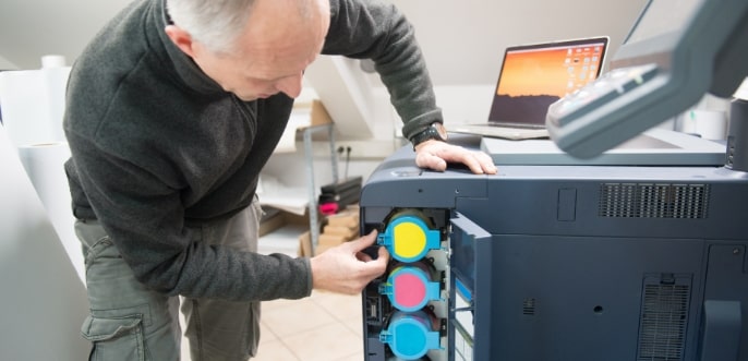 Ein IT-Techniker steht vor einem geöffneten Drucker und möchte die Farbkartuschen tauschen.